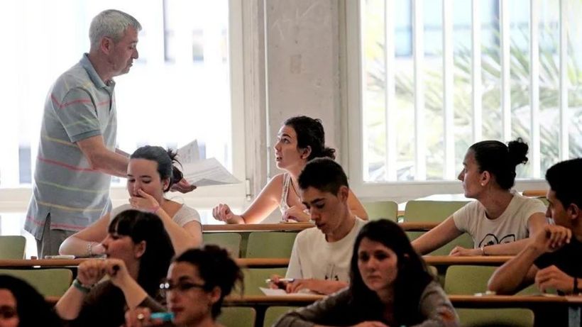un profesor repartiendo examenes y los alumnos