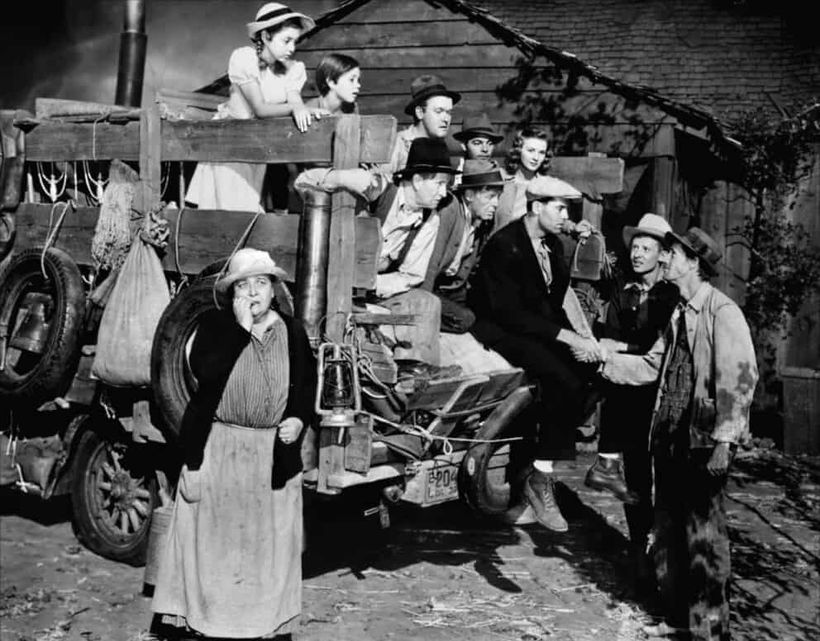 Escena en blanco y negro de Las uvas de la ira con una familia y varias personas sobre un camión de mudanza.