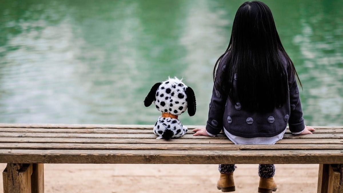 Una niña sentada junto a su peluche Una niña sentada junto a su peluche