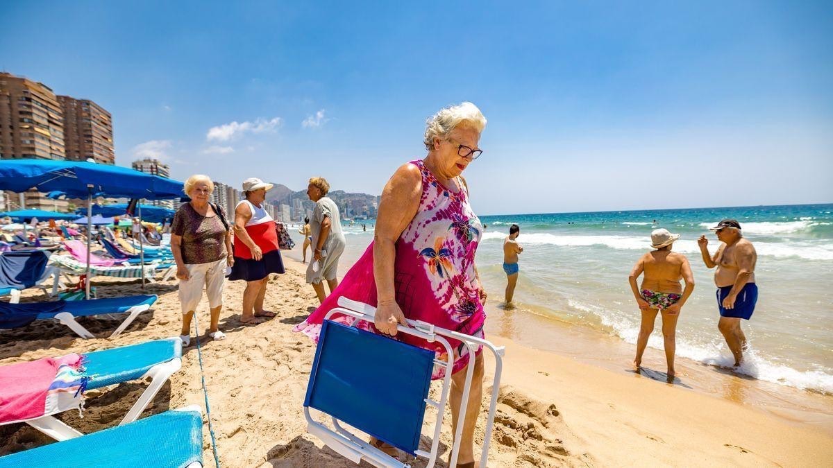 Una mujer baja a la playa con una silla.