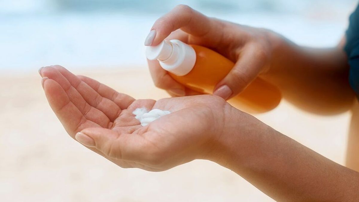 Unas manos echando crema con la playa de fondo. Manos echando crema.