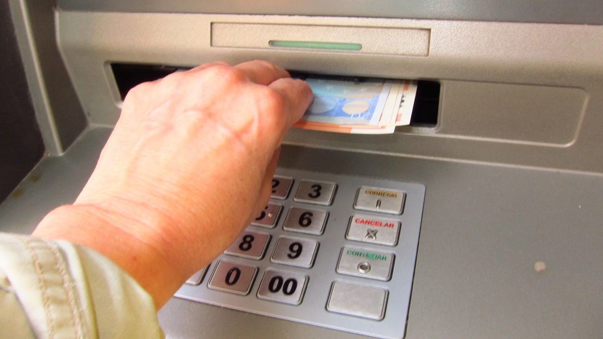 Una mano en un cajero sujetando unos billetes. Sacar dinero.