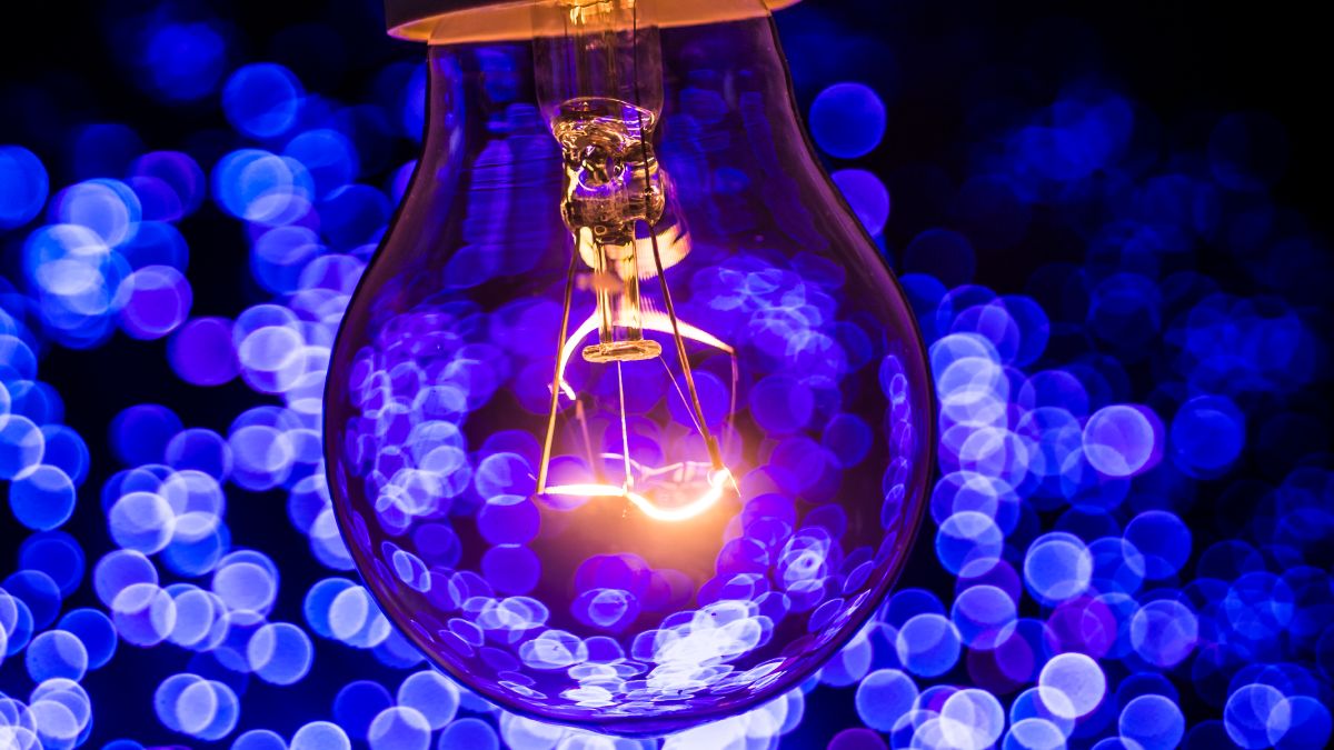 Bombilla de luz encendida, sobre fondo morado