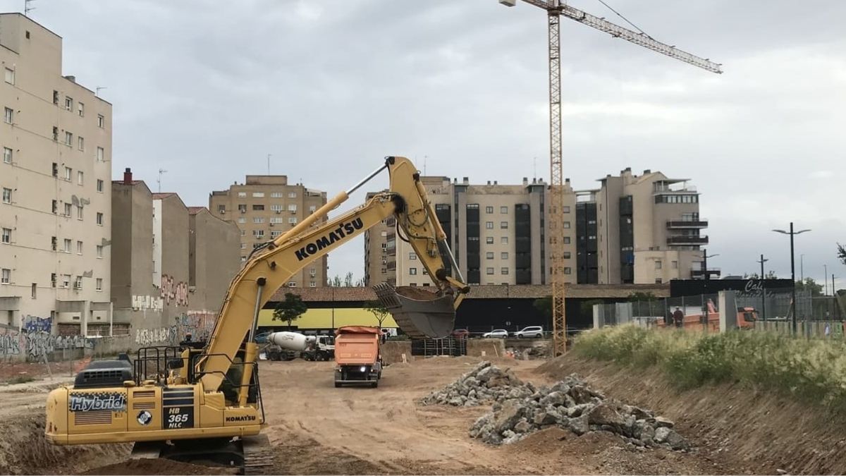 Una máquina en una obra, con varias viviendas nuevas al fondo. Obra