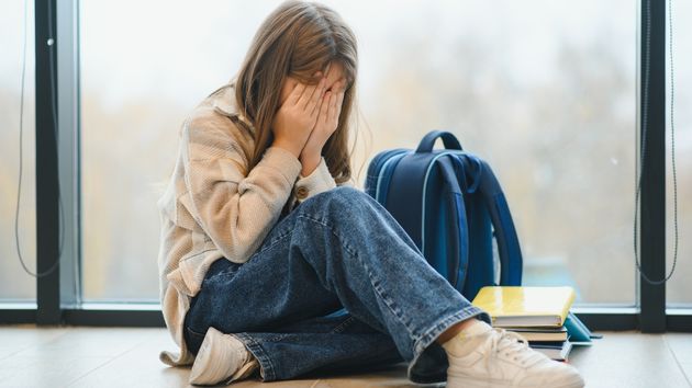 Una niña llorando con su mochila al lado