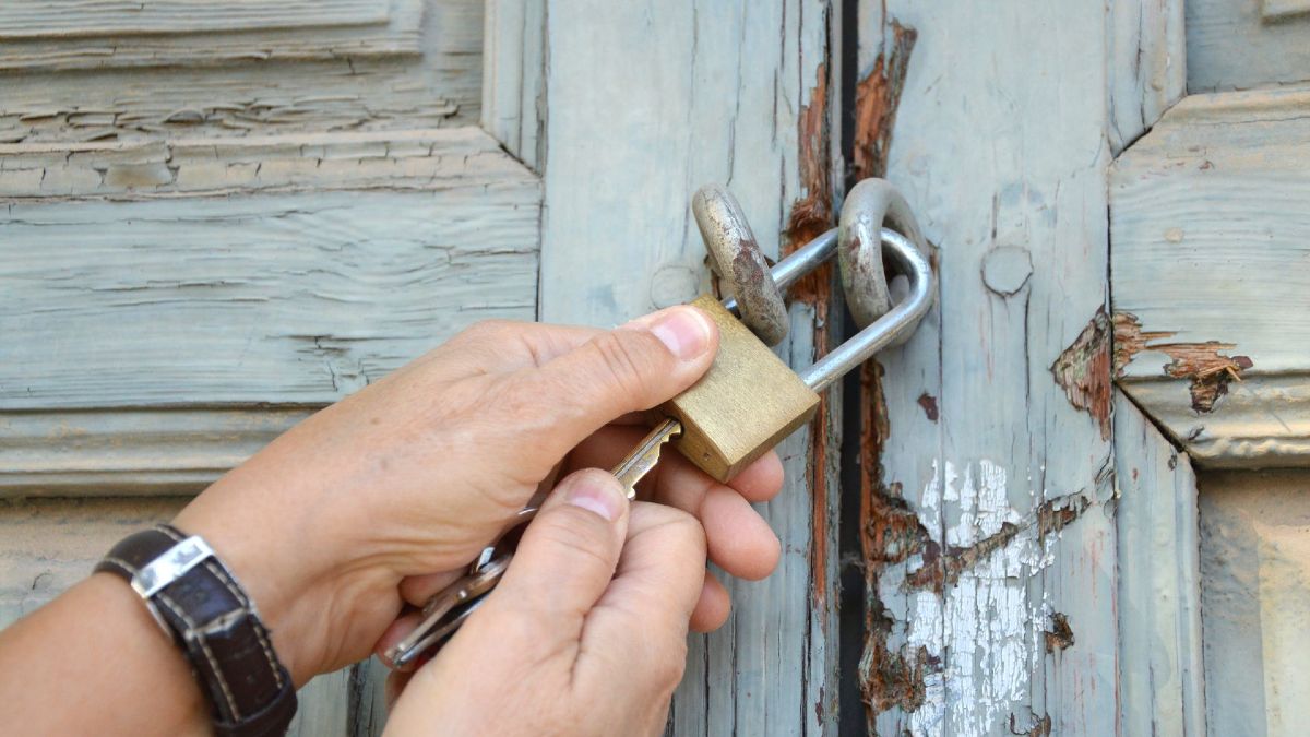 Una persona cerrando una puerta con un candado Una persona cerrando una puerta con un candado