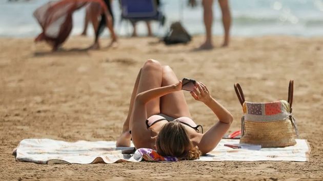 Una mujer mirando el móvil en la playa