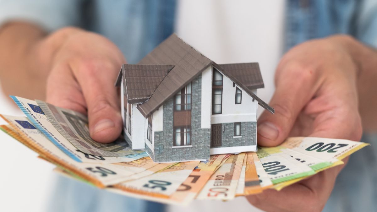 Una persona sujetando billetes de euro y la figura de una casa Una persona sujetando billetes de euro y la figura de una casa