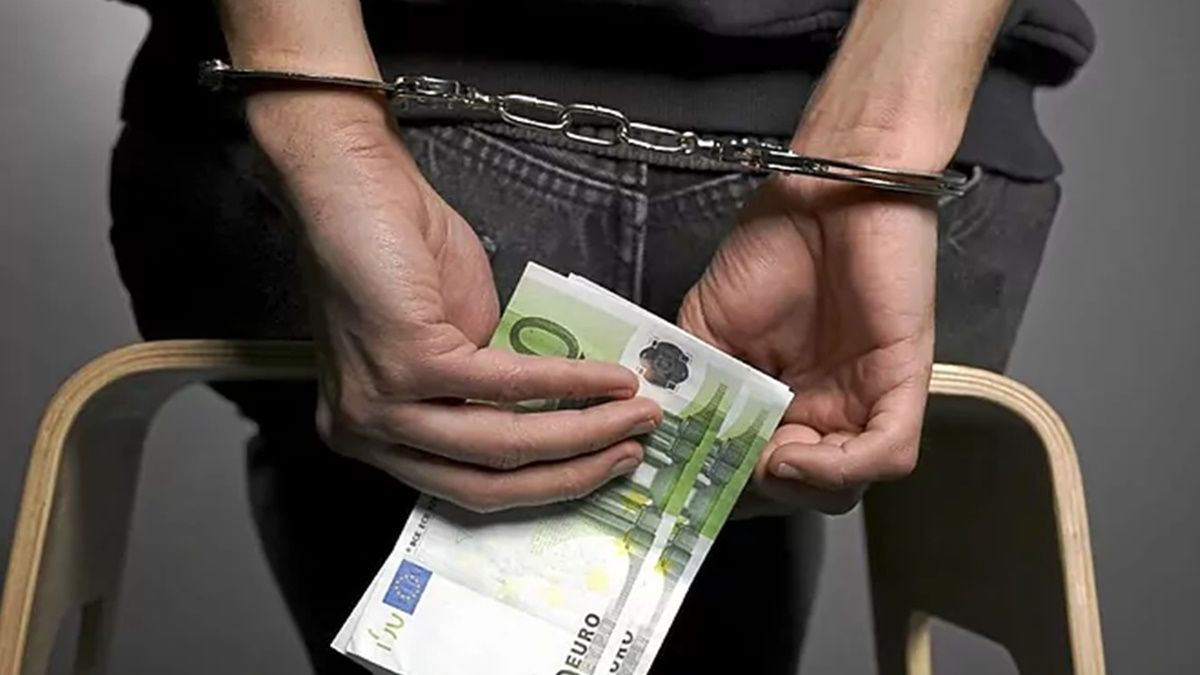 Una persona esposada sosteniendo billetes