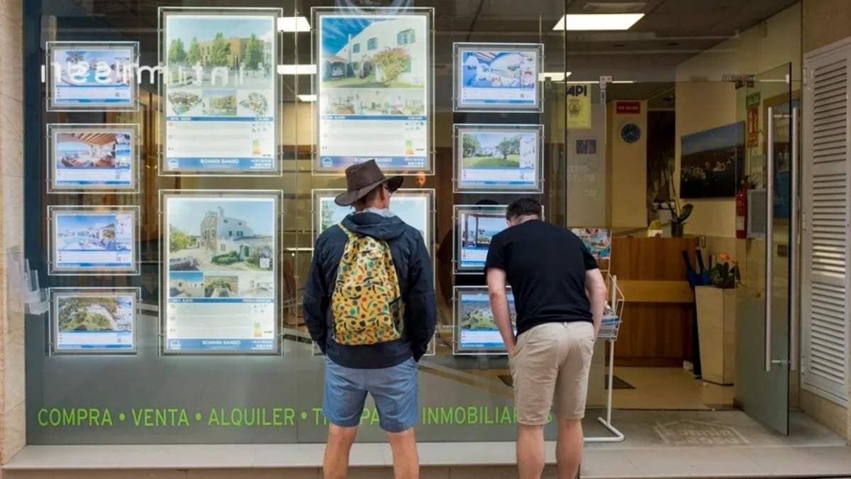 Dos personas consultando precio en la fachada de una inmobiliaria