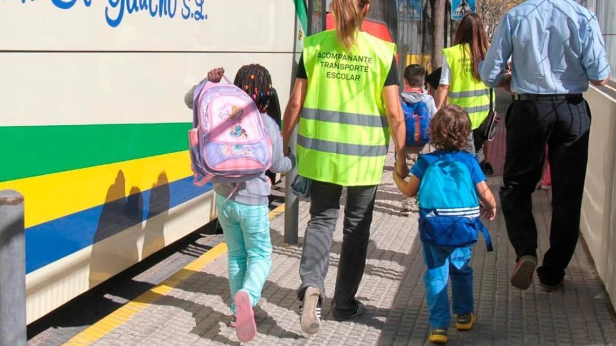 Una monitora de transporte escolar con dos niños de la mano