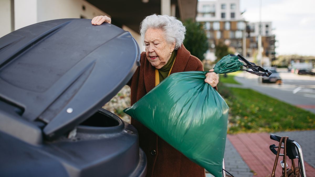 Una señora mayor tirando una bolsa al contenedor de basura