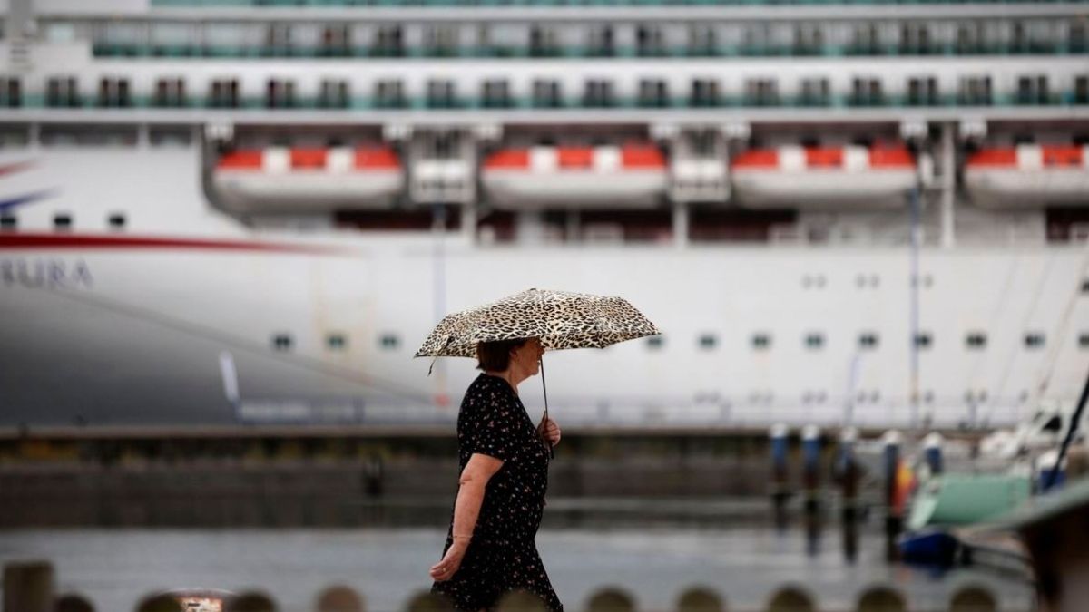 Una mujer pasea dealnte de un barco con un paraguas
