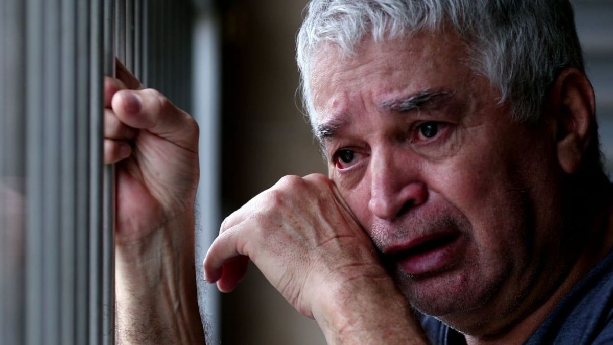 Un anciano llorando agarrado a una verja