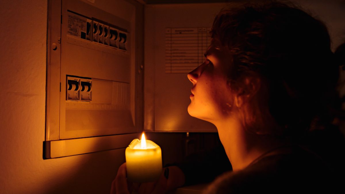 Una mujer con una vela revisando el contador de la luz