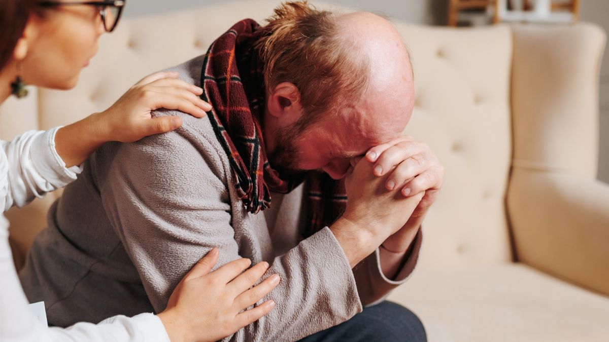 Un hombre llorando en el sofá mientras una mujer le consuela