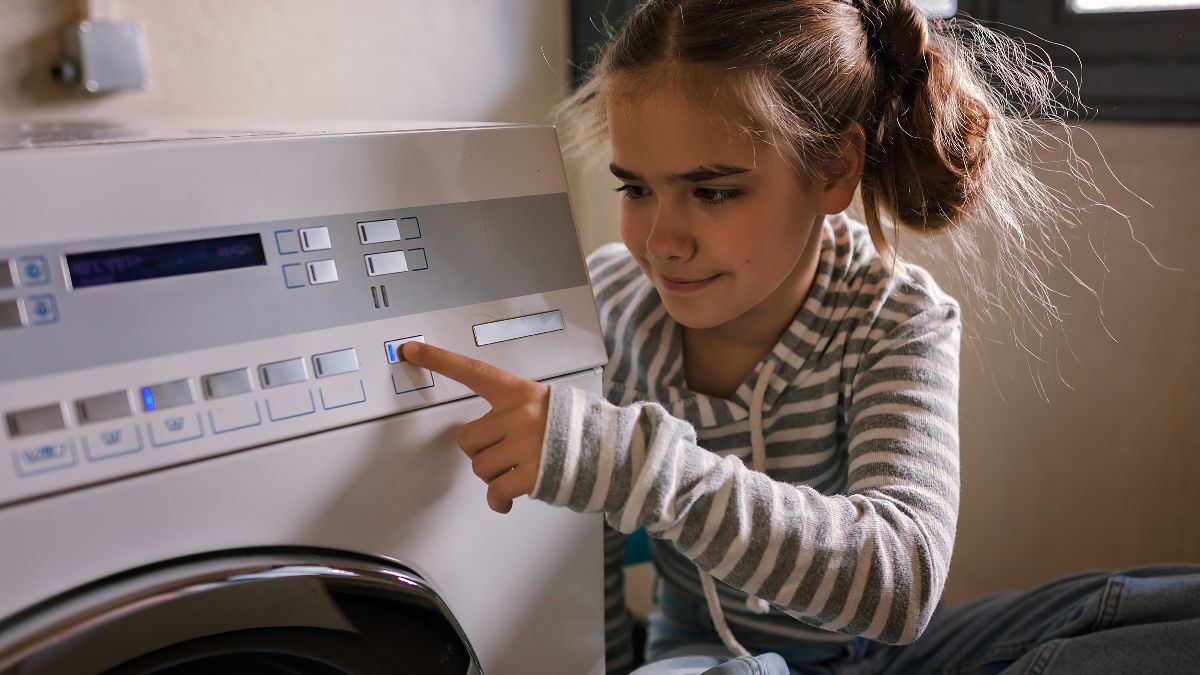 una niña apretando el botón de encender la lavadora
