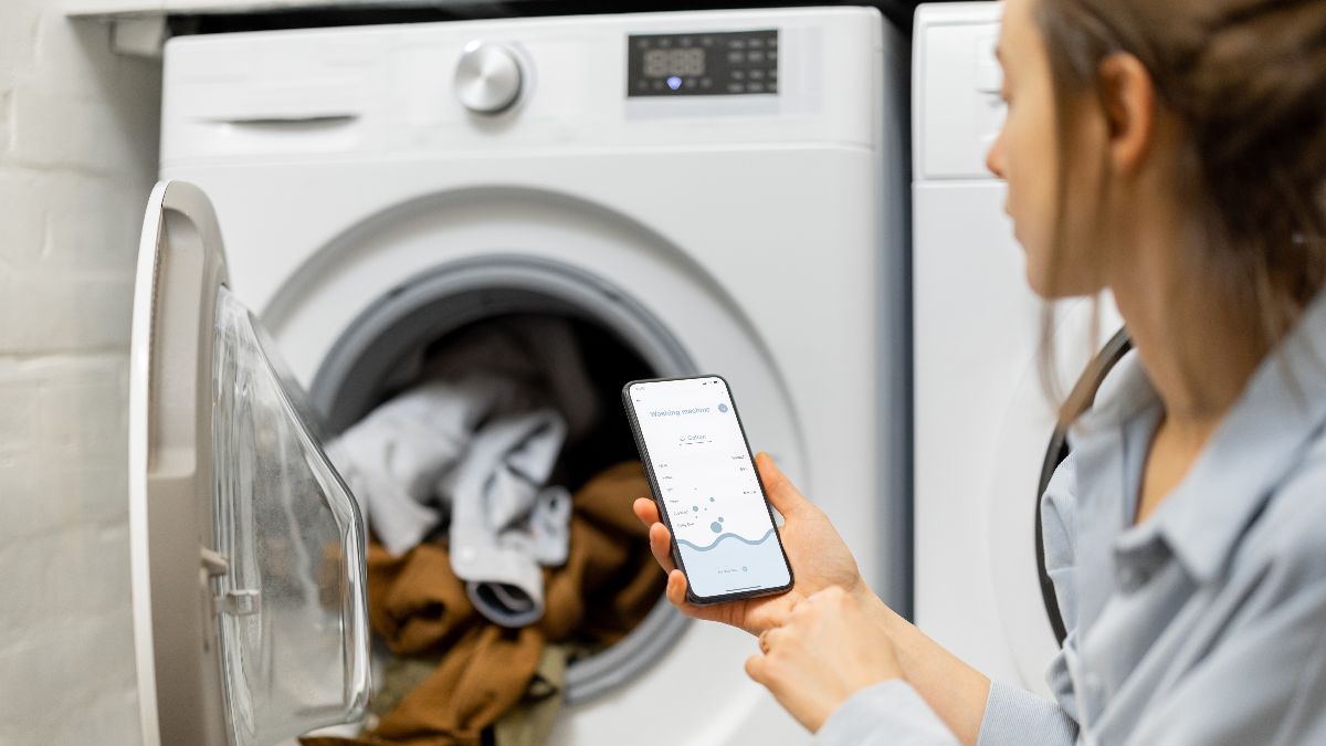 Una mujer poniendo la lavadora, mientras consulta su móvil