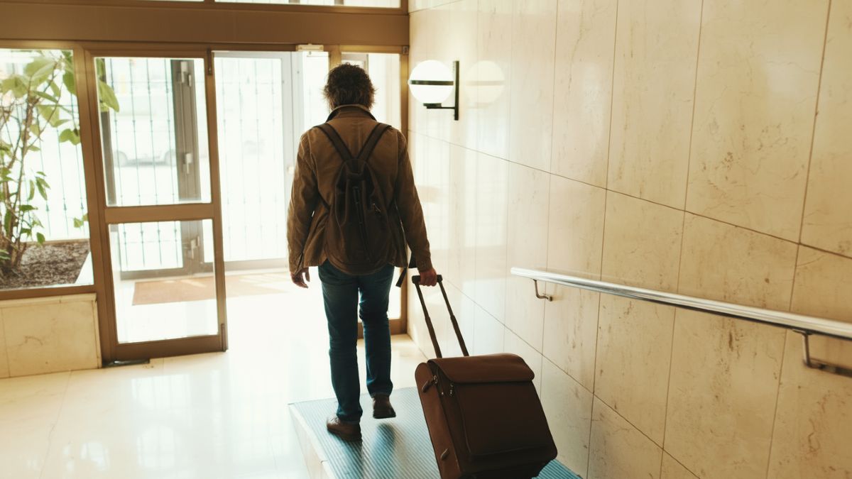 Un hombre saliendo de un edificio de viviendas con una maleta 