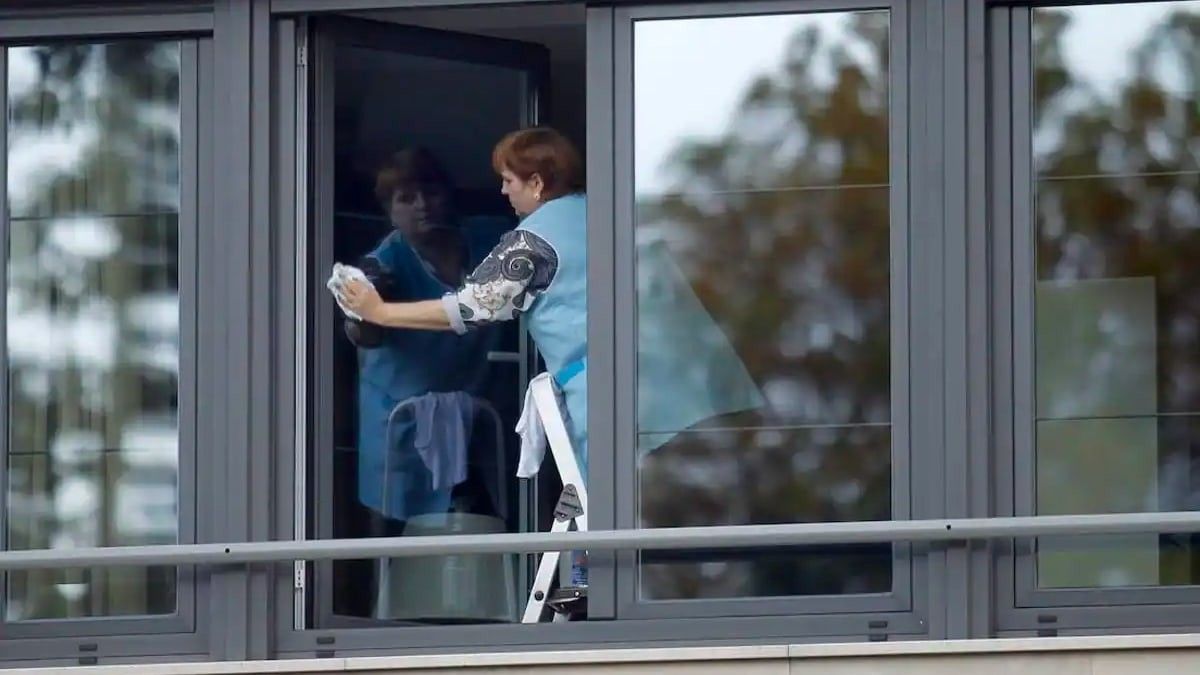 Una empleada de hogar limpiando una ventana