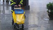 Una mujer trabajadora de Correos empuja un carrito bajo la lluvia
