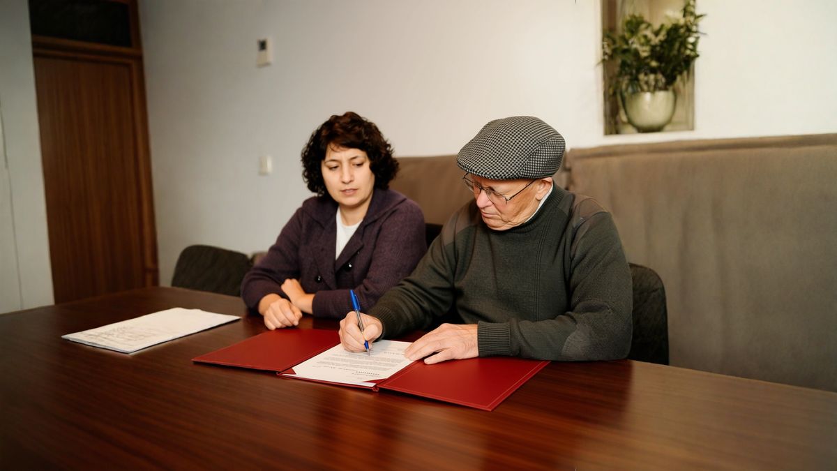 Un hombre firmando documentos junto a una mujer