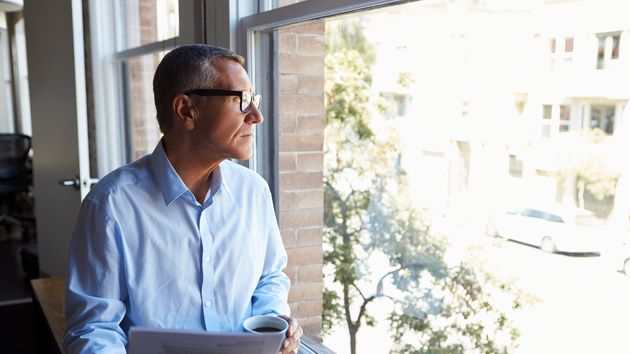 Un hombre con rostro serio mirando por la ventana de la oficina
