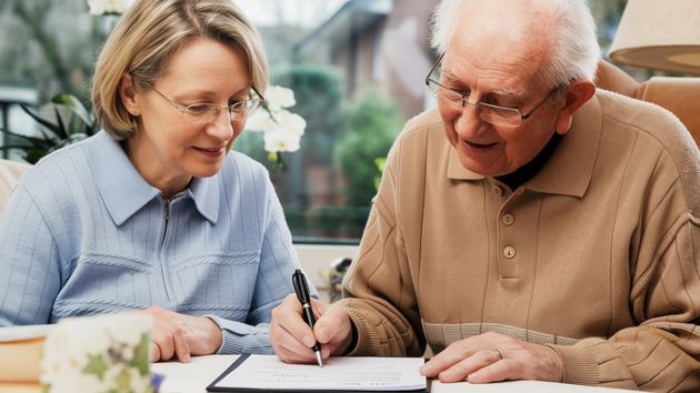 Un anciano firmando un documento junto a una mujer 