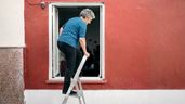 Una mujer entrando a una casa por la ventana con una escalera 