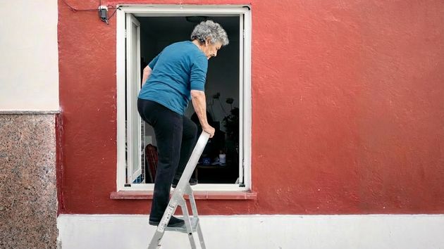Una mujer entrando a una casa por la ventana con una escalera 