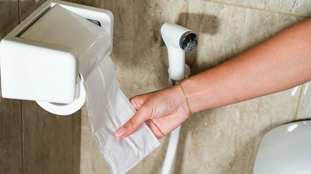 Una mujer cogiendo papel en el baño