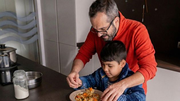 Un padre ayudando a comer a su hijo