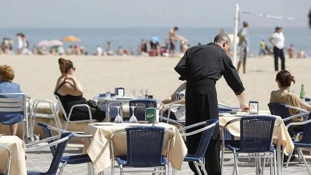 Un camarero atiende las mesas de un restaurante junto a la playa