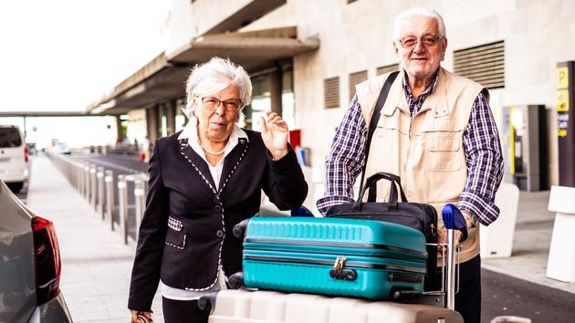 Una pareja de personas mayores con un carrito y maletas