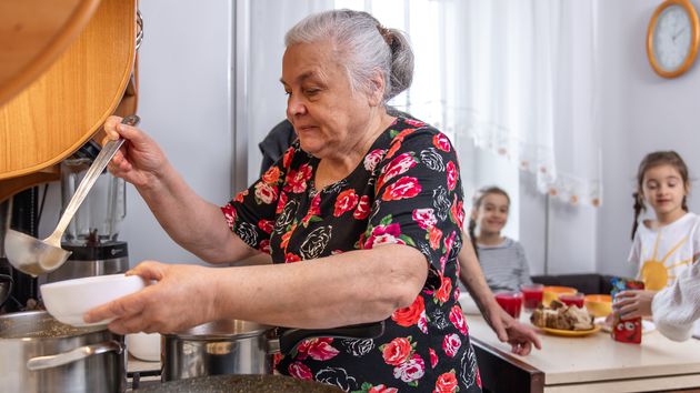 una cocinera mayor poniendo de comer a unos niños