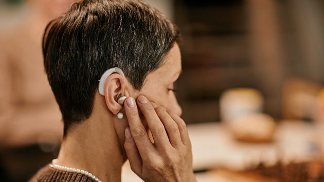Una mujer toca un audífono en su oreja