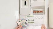 una mano sujetando una factura y unos billetes de euros en el contador de luz