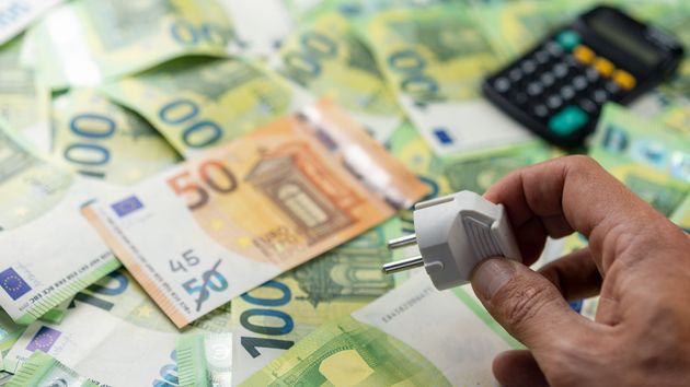 una mano con un enchufe y billetes de euros