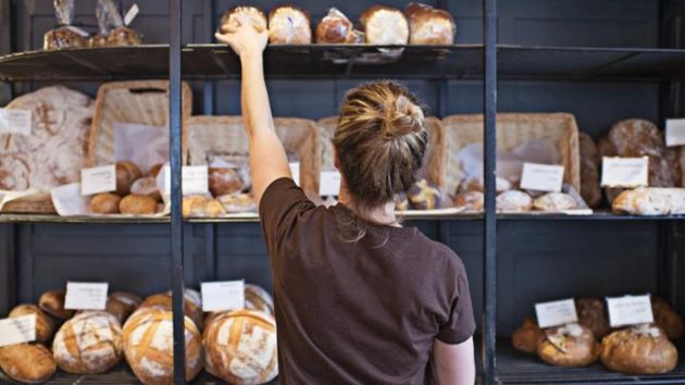 Una mujer coloca panes en su panadería