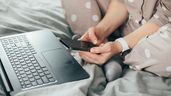 Una mujer mirando su móvil desde la cama, sin trabajar en el ordenador