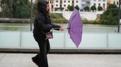Una mujer intentando protegerse de la  lluvia y el viento.