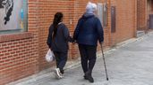 Una mujer caminando por la calle con ayuda de su cuidadora