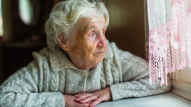 Imagen ilustrativa de una anciana triste mirando por la ventana 