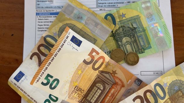 Una nómina junto a monedas y billetes de euro