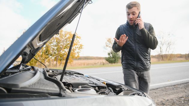 Un hombre mirando su coche averiado
