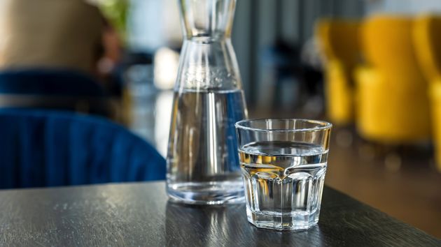 Un vaso lleno de agua, colocado en la mesa de un hotel