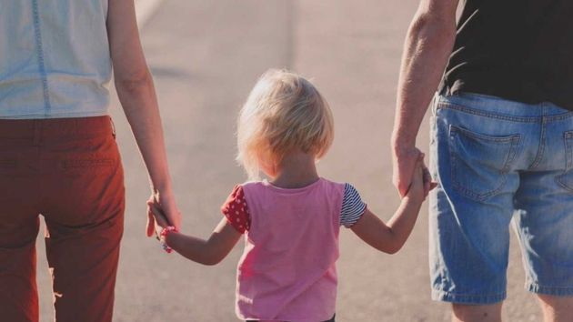 Una niña camina de la mano de sus padres