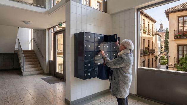 Una anciana abriendo el buzón en el portal de la comunidad de vecinos 