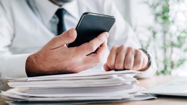 Una persona revisando el móvil junto a varios documentos de trabajo
