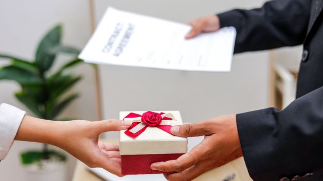 un trabajador recibiendo un regalo con contratos y documentos en la otra mano